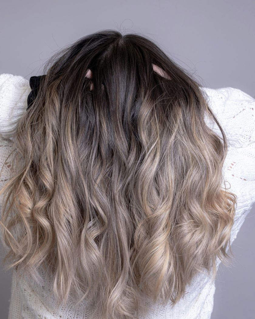 Bølget hår med balayage fra mørkt til lyst, sett bakfra mot en lilla vegg